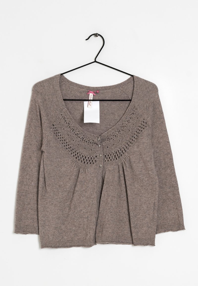 Brun stickad cardigan med långa ärmar, dekorativt virkade mönster runt halsringningen och knappar framtill, hängande på en svart galge.