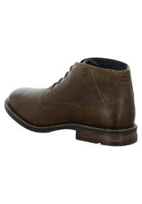 Botas de cuero marrón hasta el tobillo con puntera redonda, cordones simples y costuras en contraste, que presentan una suela plana y una marca sutil.