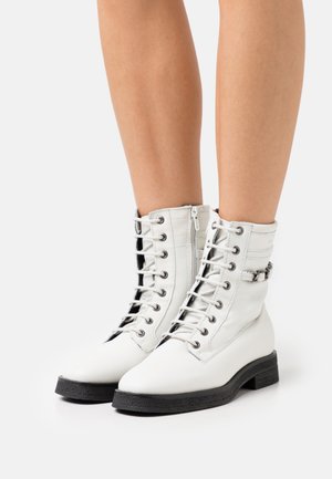 Bottes blanches en cuir à la cheville avec semelles noires, dotées de lacets, fermeture éclair et un accent en chaîne sur le dessus. Texture lisse et bout arrondi.