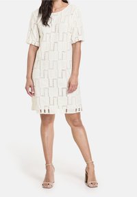 Vestido color crema hasta la rodilla con un patrón geométrico, mangas cortas y detalles recortados en el dobladillo.