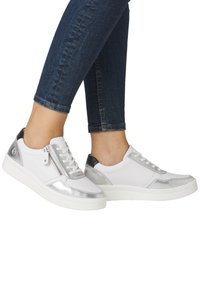 Baskets blanches avec des accents métalliques argentés et un talon noir, présentant une fermeture éclair sur le côté et du cuir texturé blanc. Semelle en caoutchouc.