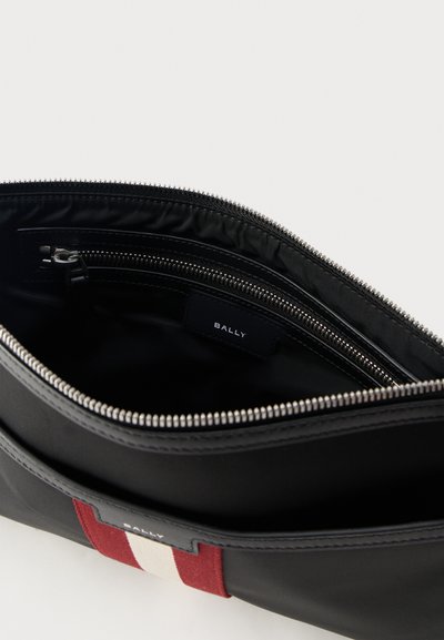 Sac Bally noir avec fermeture éclair ouverte montrant une poche intérieure zippée et un détail de bande de tissu rouge et blanc à l'extérieur.