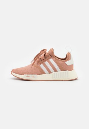 Jasnobrązowy sportowy but z białymi paskami, sznurowanym zapięciem, amortyzowaną podeszwą i pętelką na pięcie na jednolitym białym tle.