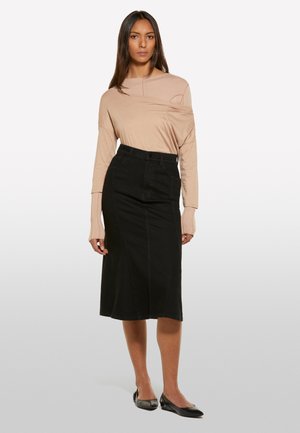Haut à manches longues beige clair avec un décolleté drapé, associé à une jupe crayon en denim noir taille haute. Des chaussures plates noires complètent la tenue.