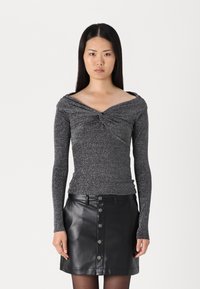 Long-sleeve, silver speckled top with a twisted neckline, paired with a black leather skirt featuring a front button detail.