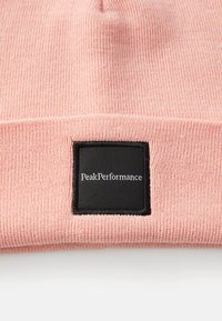 Roze gebreide beanie met een gestructureerd ribpatroon, afgewerkt met een zwart vierkant label met daarop "PeakPerformance" in witte tekst.