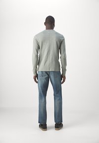 Långärmad, ljusgrå skjorta med rund hals, i kombination med blå denimjeans. Skjortan har en sömdetalj längs ryggen.