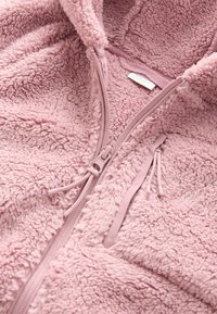 Vaaleanpunainen fleecehuppari vetoketjulla, pehmeällä tekstuurilla, kokopitkällä vetoketjulla, kiristysnauhalla ja pienellä sisätarralla.