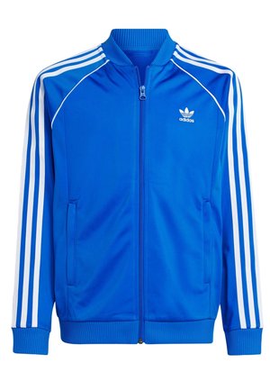 Modrá sportovní bunda Adidas s bílými třemi pruhy na rukávech, předním zipem, žebrovaným límcem, manžetami, pasem a logem na levé straně hrudi.