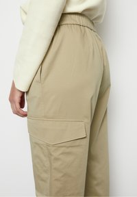 Beige cargobroek met een elastische taille, voorzien van een ruime patchzak aan de zijkant, gemaakt van een soepele, lichte stof.