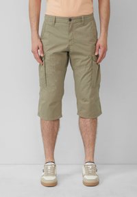 Shorts cargo beige avec une longueur jusqu'aux genoux, fabriqués en tissu léger. Présente des poches latérales et un motif texturé. Portés avec des baskets beiges.