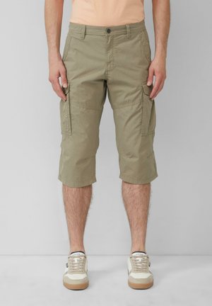 Beige cargoshorts met een knielange zoom, gemaakt van lichte stof. Beschikt over zijzakken en een gestructureerd patroon. Draagt een paar beige sneakers.