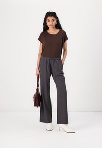 Haut marron à manches courtes associé à un pantalon gris taille haute. Porté avec des bottes à talons blanches et tenant un sac bordeaux. Design simple et moderne.