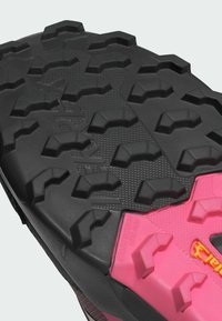 Schwarze und rosa Trail-Schuhsohle mit einem robusten Profilmuster, ausgeprägten Stollen für Traktion, texturiertem Oberflächenmaterial und verstärkten Rändern.