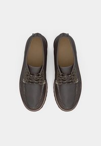 Brune skinnsko med rund tå, kontrasterende sømmer og fire snøringer. Sålene er av gummi med en lett avrundet kant.