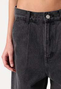 Zwarte denimshorts met een hoge taille, voorzien van een knoopsluiting en subtiele textuur. De stof heeft een vleugje glans en opvallende stiksels.