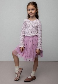 Biała bluzka z długim rękawem w różowy kwiatowy wzór, zestawiona z warstwową różową spódnicą z tiulu z motylowymi akcentami oraz brązowymi butami na paski.