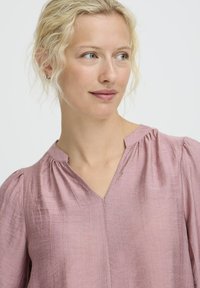 Helles rosa Bluse aus strukturiertem Stoff, mit V-Ausschnitt, gerafften Schultern und subtilen Nähten.
