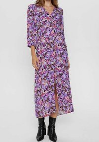 Blommig klänning i lila med puffärmar, V-ringning och en framklippt slits. Har en blandning av rosa, lila och svarta blommor på en ljus bakgrund.