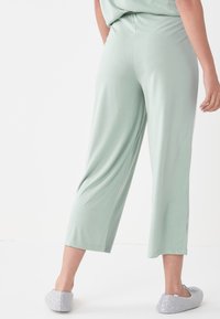 Lichtgroene, rekbare cropped pants met een relaxed fit, voorzien van een tailleband en een gladde textuur. Gecombineerd met grijze fluffy instappers.