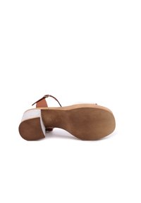 Scarpa con tacco con un cinturino in pelle beige, parte superiore in suede bianco e suola in gomma. Presenta un tacco spesso e un fondo texturizzato per una migliore aderenza.