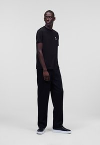 Zwarte katoenen t-shirt met korte mouwen en een kleine graphic op de linkerkant van de borst, gecombineerd met losse zwarte broeken en zwarte sneakers.