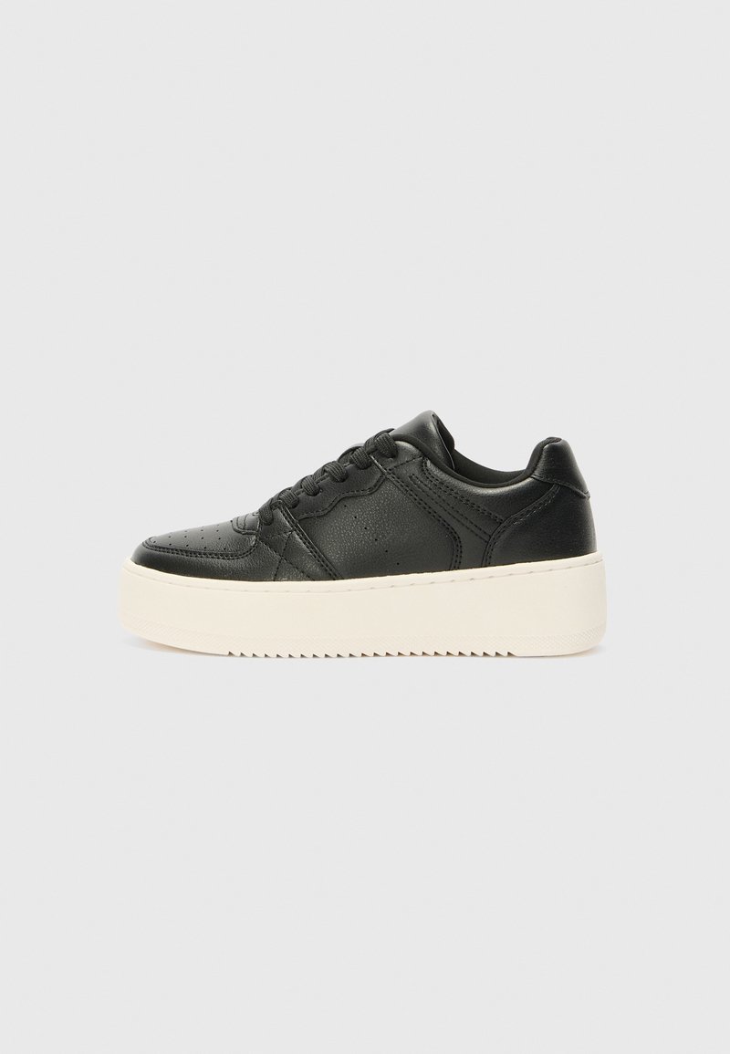 Baskets en cuir noir avec une épaisse semelle plateforme blanche et des lacets noirs, vues de côté sur un fond gris clair uni.