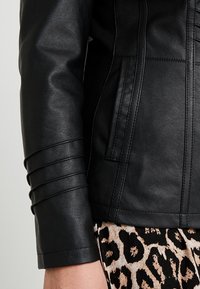 Zwarte neplederen jas met strakke mouwen, horizontale stiksels en een asymmetrische rits. Gecombineerd met een broek met luipaardprint.