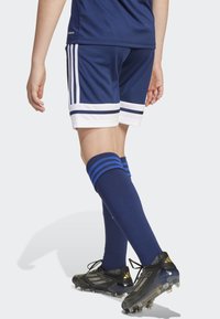 Navy idrottsshorts med vita och navy-randiga detaljer, blå knähöga strumpor med tre ränder, och svarta fotbollsskor med guldiga accenter.