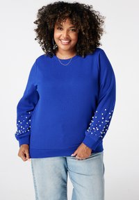 Blauwe sweatshirt met een relaxte pasvorm, voorzien van parelaccenten op de mouwen. Het materiaal lijkt zacht; het ontwerp bevat ribgebreide manchetten en een halslijn.