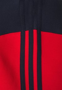 Sudadera roja y azul marino con una textura suave, diseño a bloques de color y tres rayas verticales azul marino en el pecho.