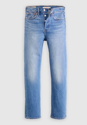 Lyseblå jeans med lige ben, knaplukning, fem lommer og diskret falmning på lårene mod en ensartet lys baggrund.