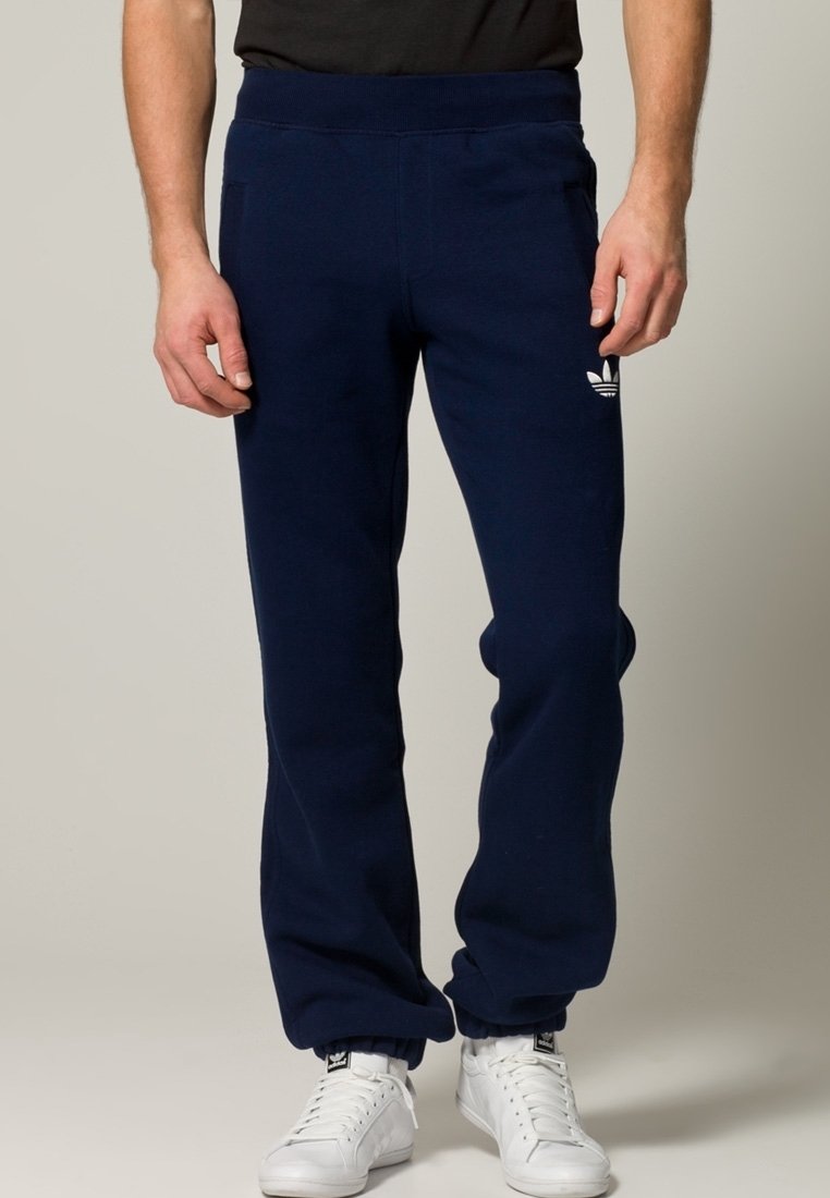 Mörkblåa sweatpants med mjuk textur, utrustade med elastisk midja och muddar, samt en vit Adidas-logga på vänstra låret.