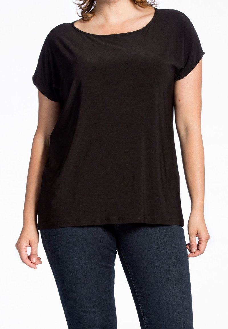 Haut noir à manches courtes en tissu doux et extensible. Il présente un col arrondi et une coupe ample, associé à un jean bleu foncé.