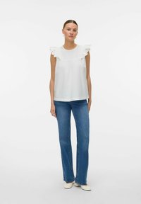 Haut sans manches blanc avec des accents à volants et des détails en œillets, associé à un jean évasé bleu et des chaussures claires. Design simple et aérien.
