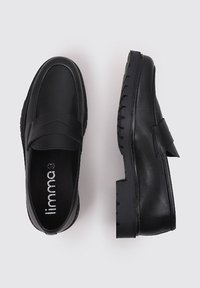 Mocasines de cuero negro con suela de goma, presentan un diseño cosido y una banda ancha en la parte superior. Textura suave, con un detalle mínimo.