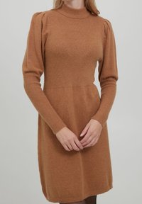 Abito lavorato a maglia marrone con colletto alto, texture a coste, maniche a palloncino e un corpetto aderente che passa a un orlo della gonna svasato.