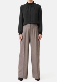 Svart långärmad blus med rynkad halsringning, parat med högmidjade, vida rutiga byxor i bruna och krämfärgade nyanser. Svarta spetsiga klackar.