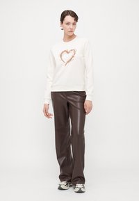 Hvite hettegensere med hjertedesign i rosegullpaljetter, kombinert med brune bukser i kunstskinn og svart-hvite joggesko.