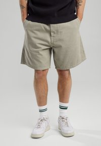 Khaki-shortsit, jotka on valmistettu puuvillasta, rento istuvuus, sivutaskut ja sileä pinta. Yhdistettynä valkoisiin lenkkareihin ja raidallisiin sukkiin.