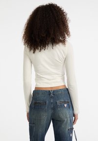 Witte langemouwen top met een cropped ontwerp, gecombineerd met donkerblauwe denim broek met zakken en een trekkoord in de taille.