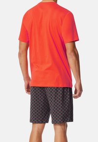 Rode katoenen t-shirt met een ronde hals, gecombineerd met zwarte shorts met een diamanten patroon in rode en grijze tinten, die een relaxte pasvorm hebben.