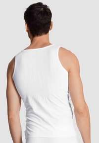 Witte tanktop met een geribbeld textuur, met een ronde halslijn en brede schouderbanden, gezien van achteren tegen een grijze achtergrond.