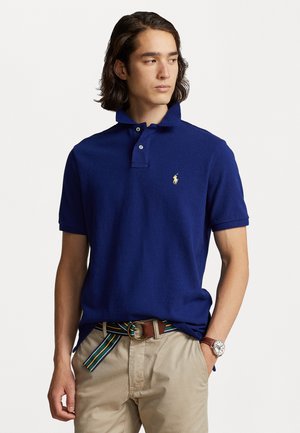 Navy blue polo shirt in a cotton fabric, featuring a classic collar, two-button placket, and a small gold logo on the chest.