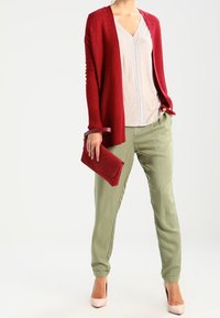 Czerwony rozpinany sweter z prążkowanym wzorem, jasnoszary top z dekoltem w serek i pionowymi paskami, oliwkowozielone zwężane spodnie oraz pasująca czerwona kopertówka.