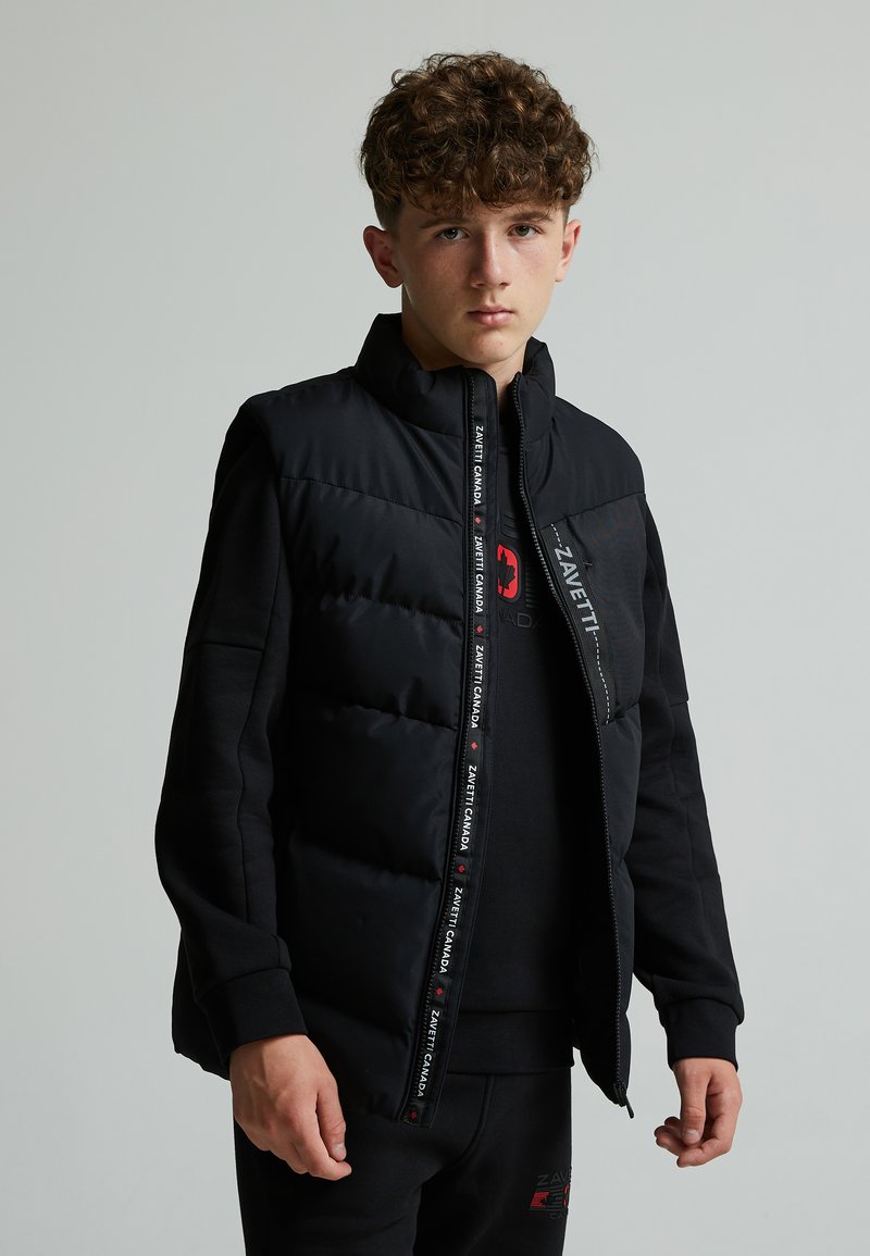 Chaqueta acolchada negra con cuello alto, cierre de cremallera y detalles de logo. La tela es suave con una sección acolchada texturizada en la parte delantera.