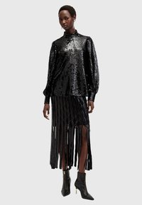 Blusa nera con paillettes e collo alto, abbinata a una gonna nera con frange caratterizzata da motivi a strati. Indossata con stivaletti neri con tacco.