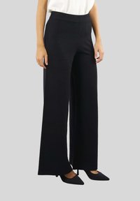 Pantaloni neri a gamba larga con vita a coste, realizzati in tessuto morbido. Presentano una texture liscia e un design lungo fino al pavimento. Indossati con tacchi neri.