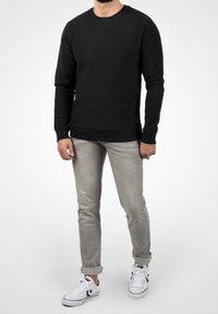 Czarna bluza z długim rękawem i okrągłym dekoltem, wykonana z fakturowanej tkaniny, zestawiona z jasnoszarymi jeansami o wąskim kroju i białymi trampkami. Prosty design, bez wzorów.