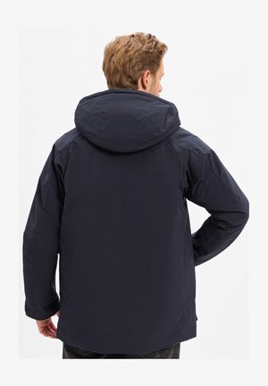 Giacca a vento blu navy con finitura liscia e opaca, caratterizzata da una vestibilità rilassata e un design semplice. Nessun logo o motivo visibile.